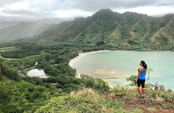 Woman overlooking cove beach surrounded by mountains - unique things to do in Oahu